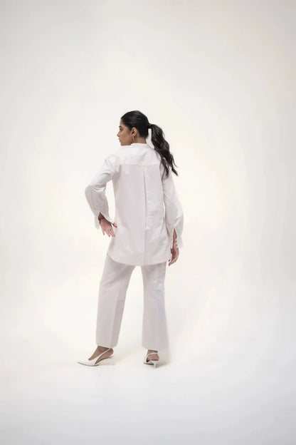 The model in a white shirt and trousers, striking a confident pose with one hand resting on her hip, facing the camera.