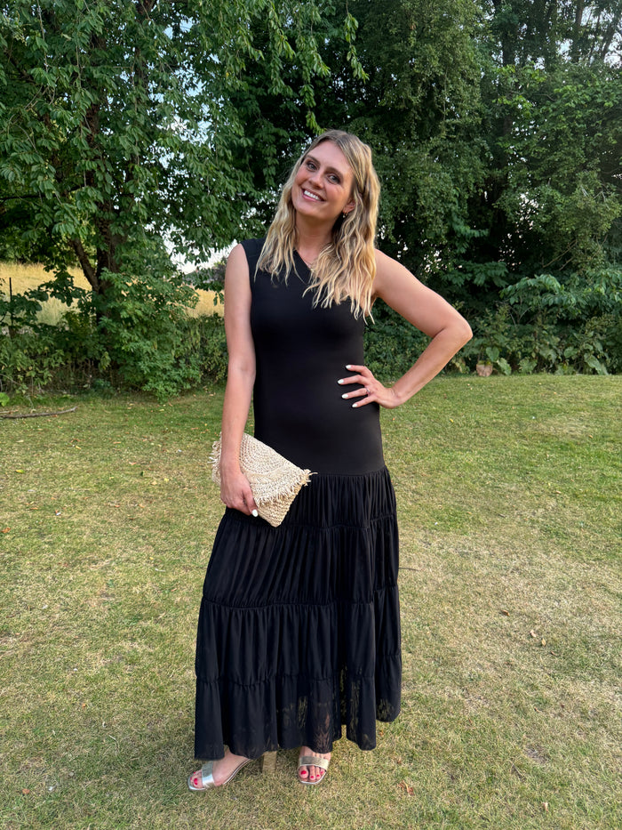 Woman in a black dress standing on grass with trees in the background wearing large sized womens shoes