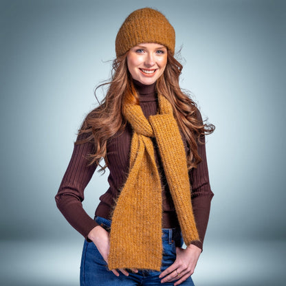 Woman wearing a mustard yellow knit hat and scarf against a gray background