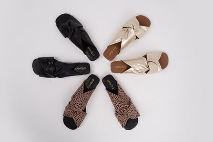 Set of black, blush cheetah, and gold flat sandals with bow details on a light gray background in large womens sizes