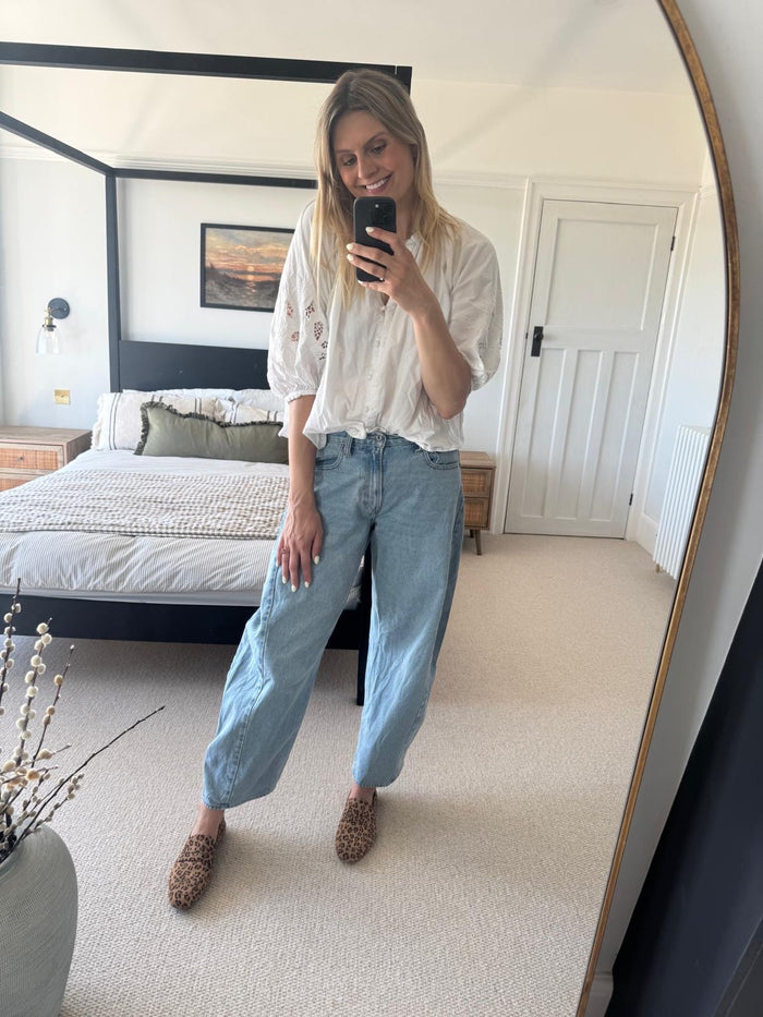 Woman taking a mirror selfie in a bedroom wearing a white blouse and blue jeans wearing large sized womens shoes