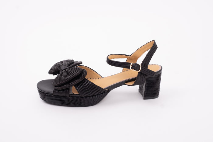 Side profile of womens heeled shoe Rhian in black. With strap and front bow detail. Available in European sizes 42-46